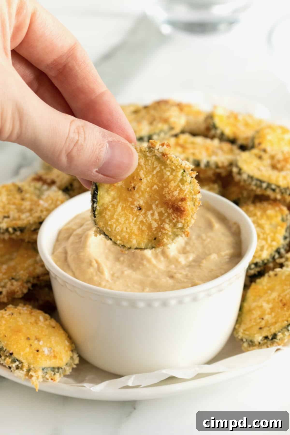 Crispy Zucchini Snacks 3 An oblong white serving platter of zucchini chips surrounding a bowl of hummus.