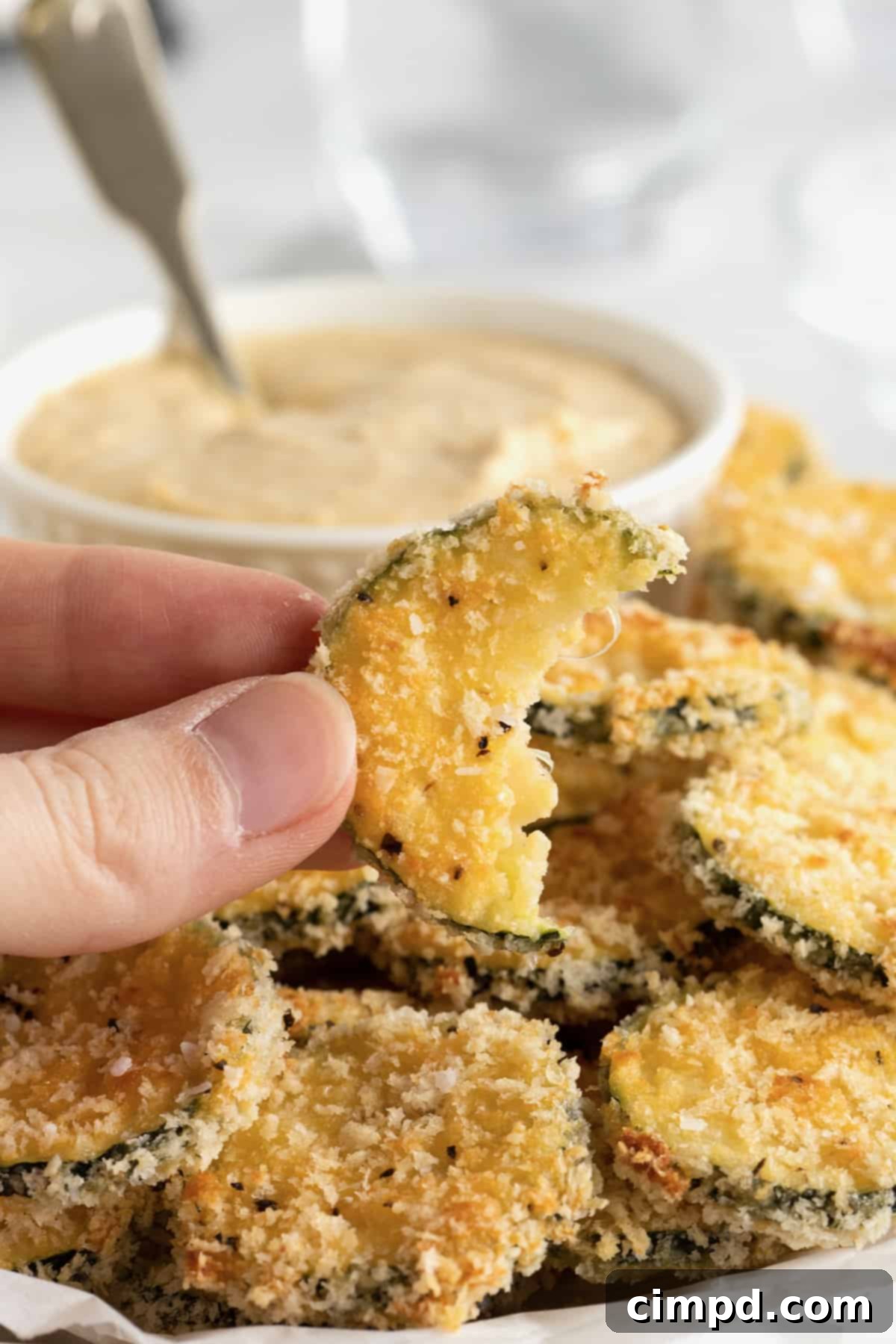 Crispy Zucchini Snacks 4 An oblong white serving platter of zucchini chips surrounding a bowl of hummus with a spoon in it.
