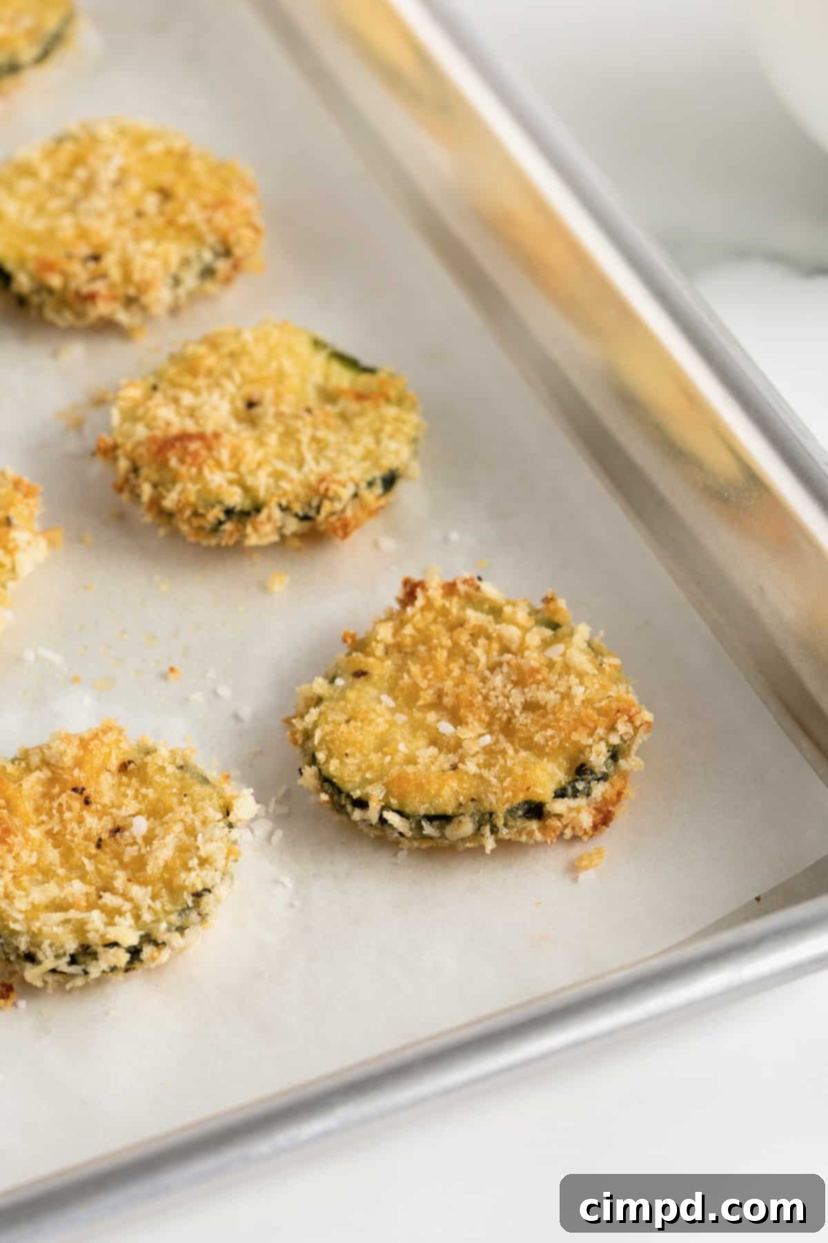 Crispy Zucchini Snacks 9 The corner of an aluminum baking sheet with four zucchini chips.