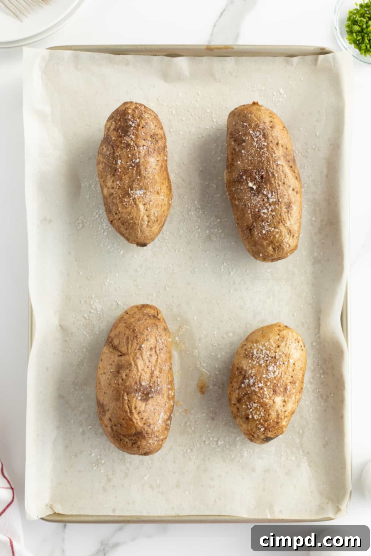 Baked potatoes cooking in the oven on a baking sheet, by The BakerMama.