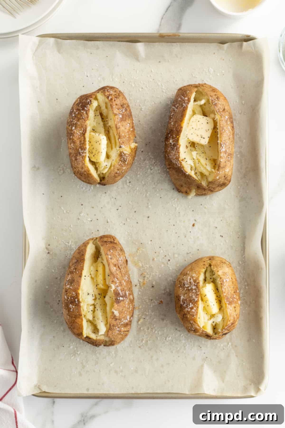 A perfectly baked potato, split open and topped with butter, ready to be customized, by The BakerMama.