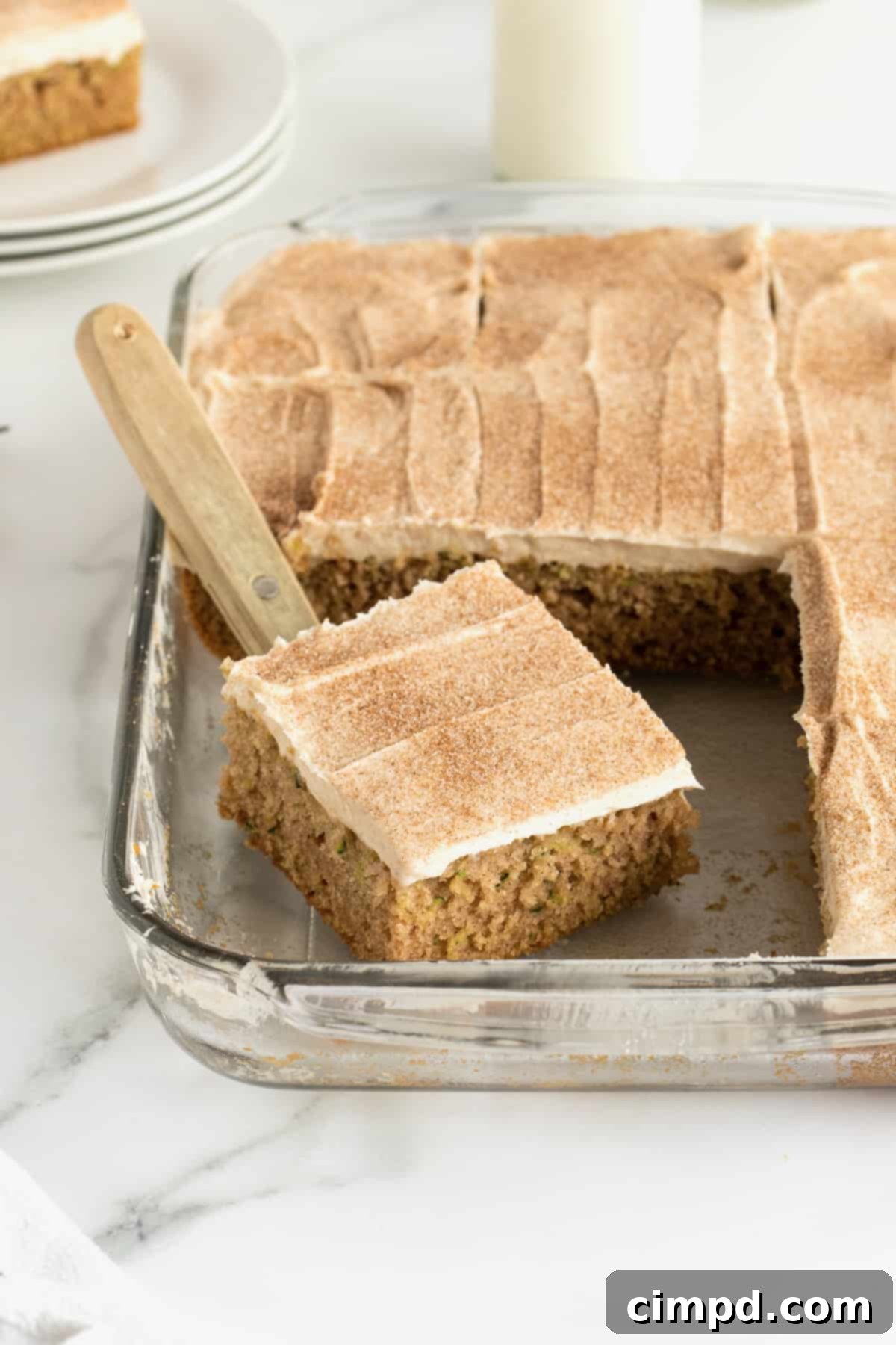 A zucchini sheet cake in a glass dish with cinnamon cream cheese frosting, ready to be served.