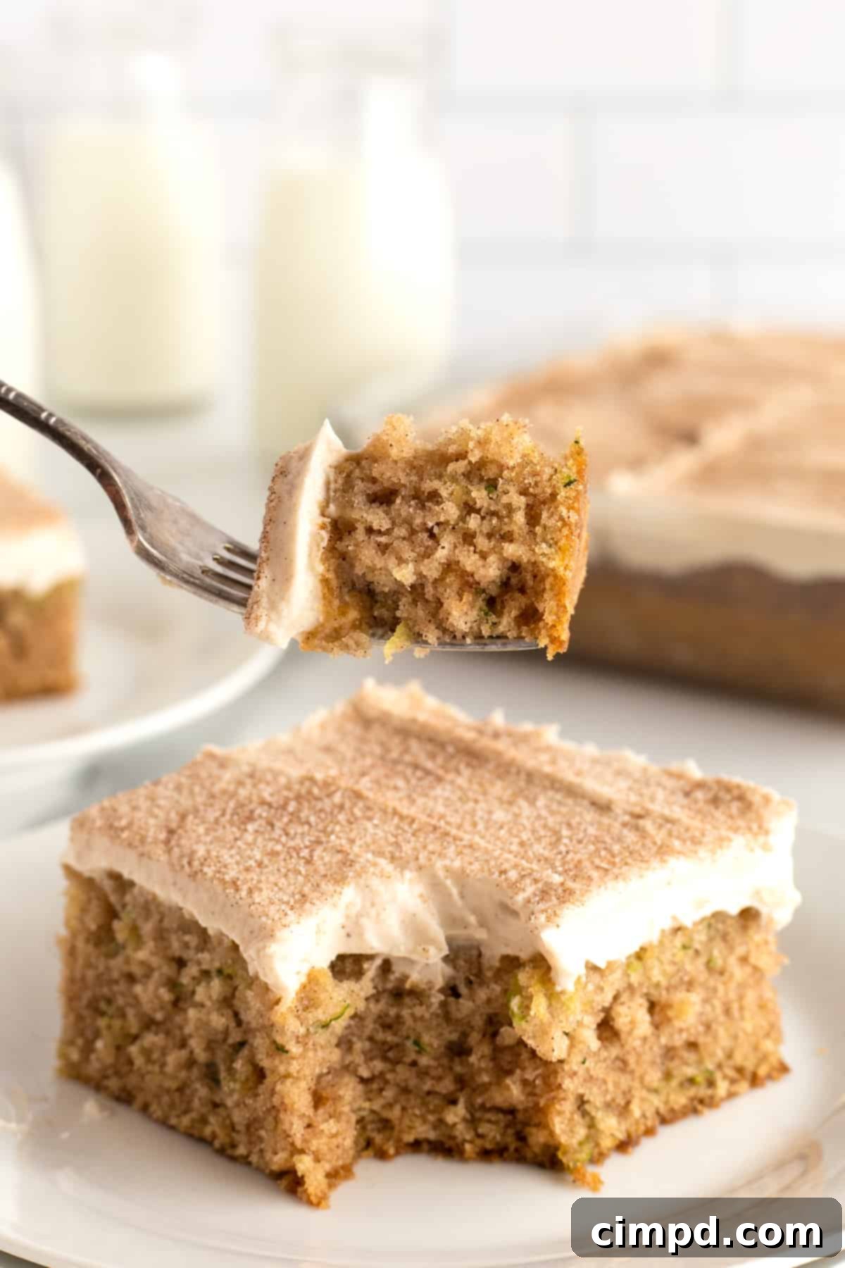 A perfectly sliced piece of zucchini cake, revealing its moist interior, topped with thick cinnamon cream cheese frosting and served on a white plate.