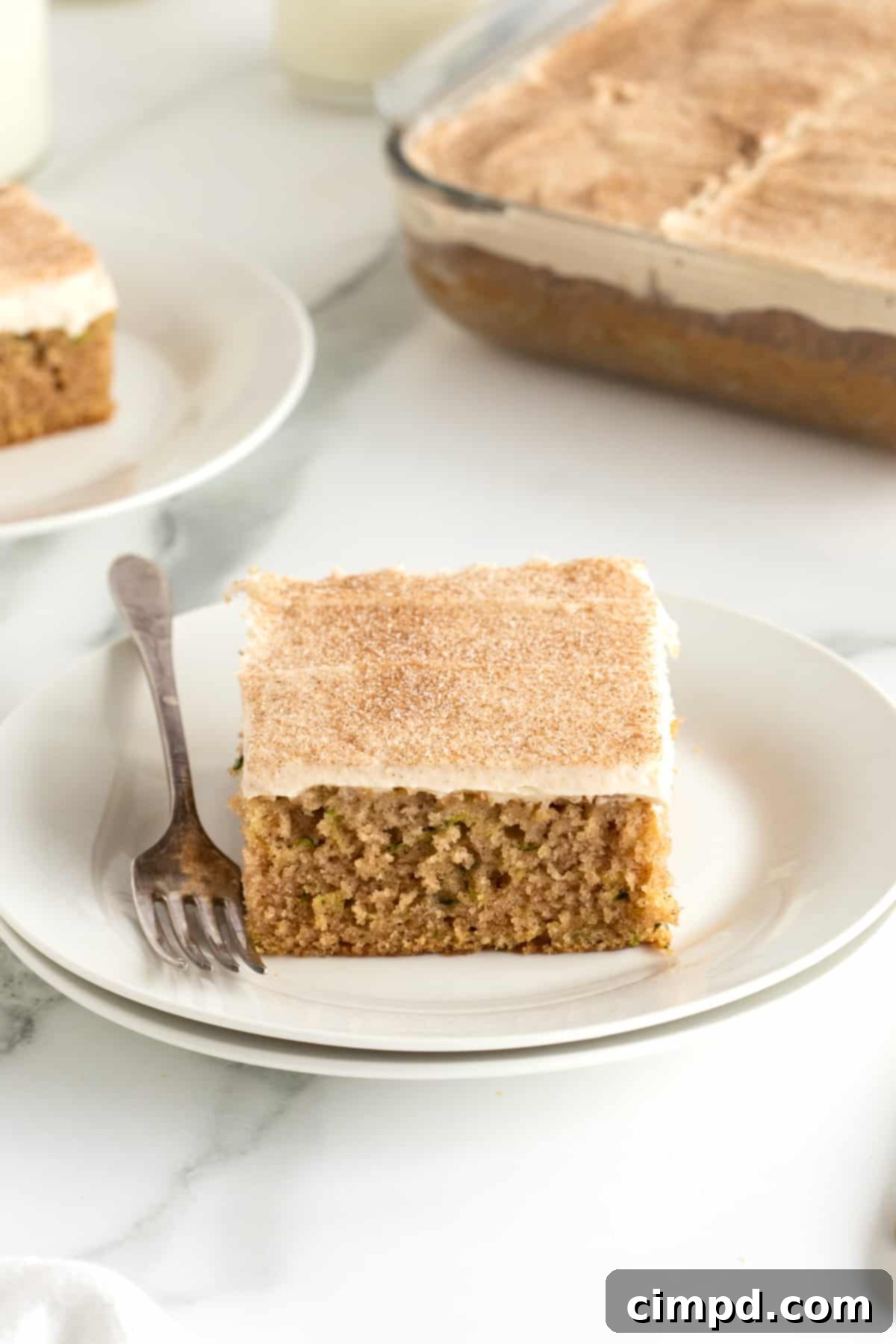 A close-up of a slice of zucchini cake with a generous layer of cinnamon cream cheese frosting, served on a pristine white plate.
