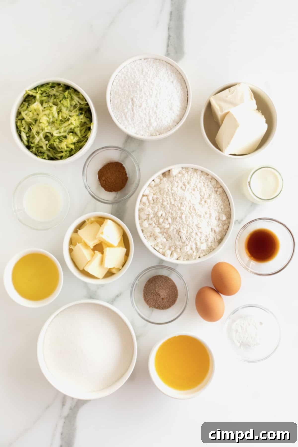 Individual bowls holding key ingredients for zucchini cake: shredded zucchini, flour, vanilla extract, cream cheese, butter, baking powder, and cinnamon, alongside two large brown eggs.