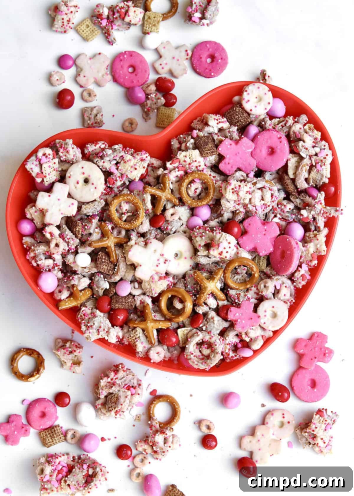 A vibrant, heart-themed XOXO Valentine's Day Snack Mix spread out on parchment paper, featuring pink, red, and white candies, cereals, and pretzels.