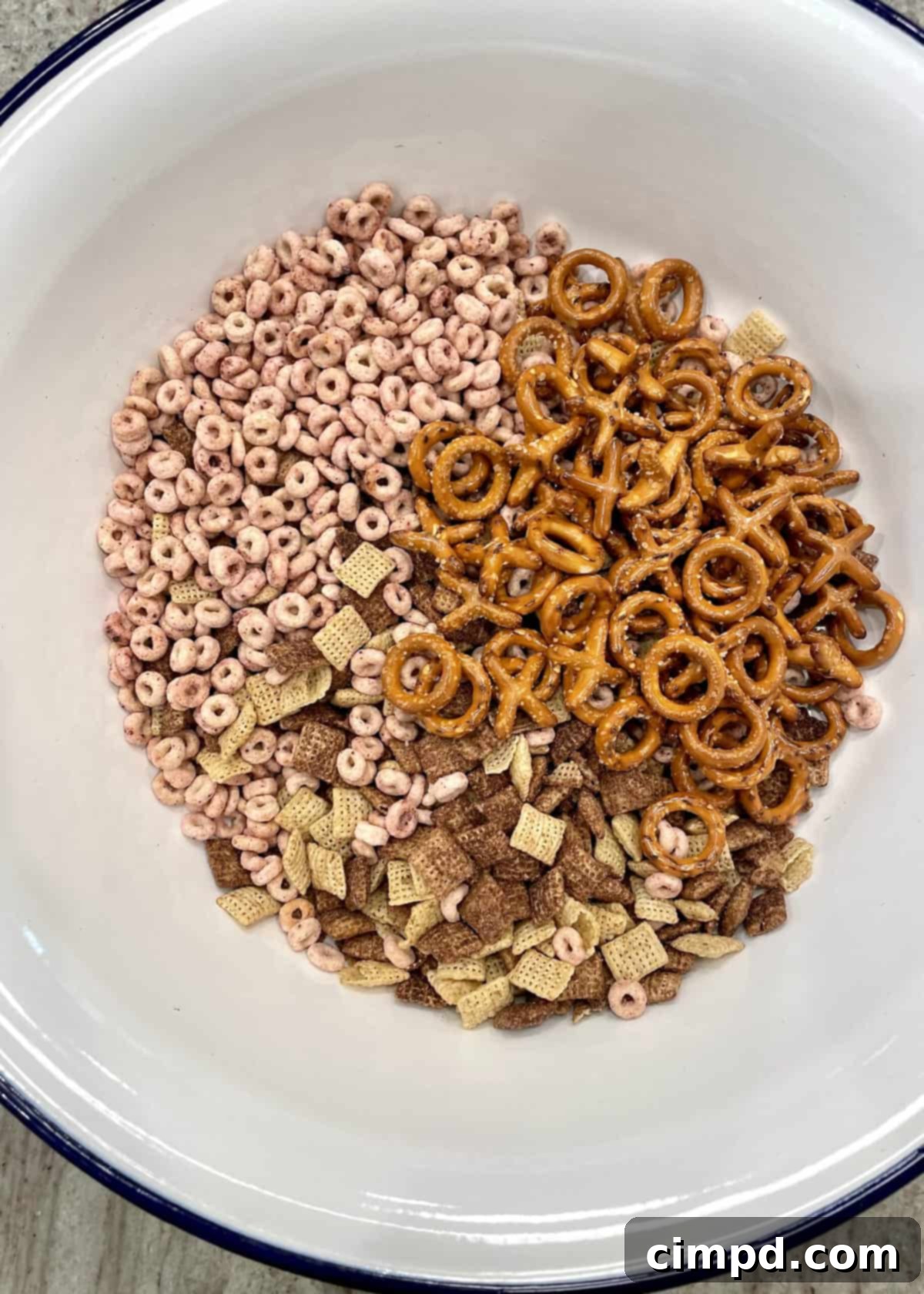 Initial dry ingredients for XOXO Valentine's Day Snack Mix, including cereals and pretzels, mixed in a large bowl.