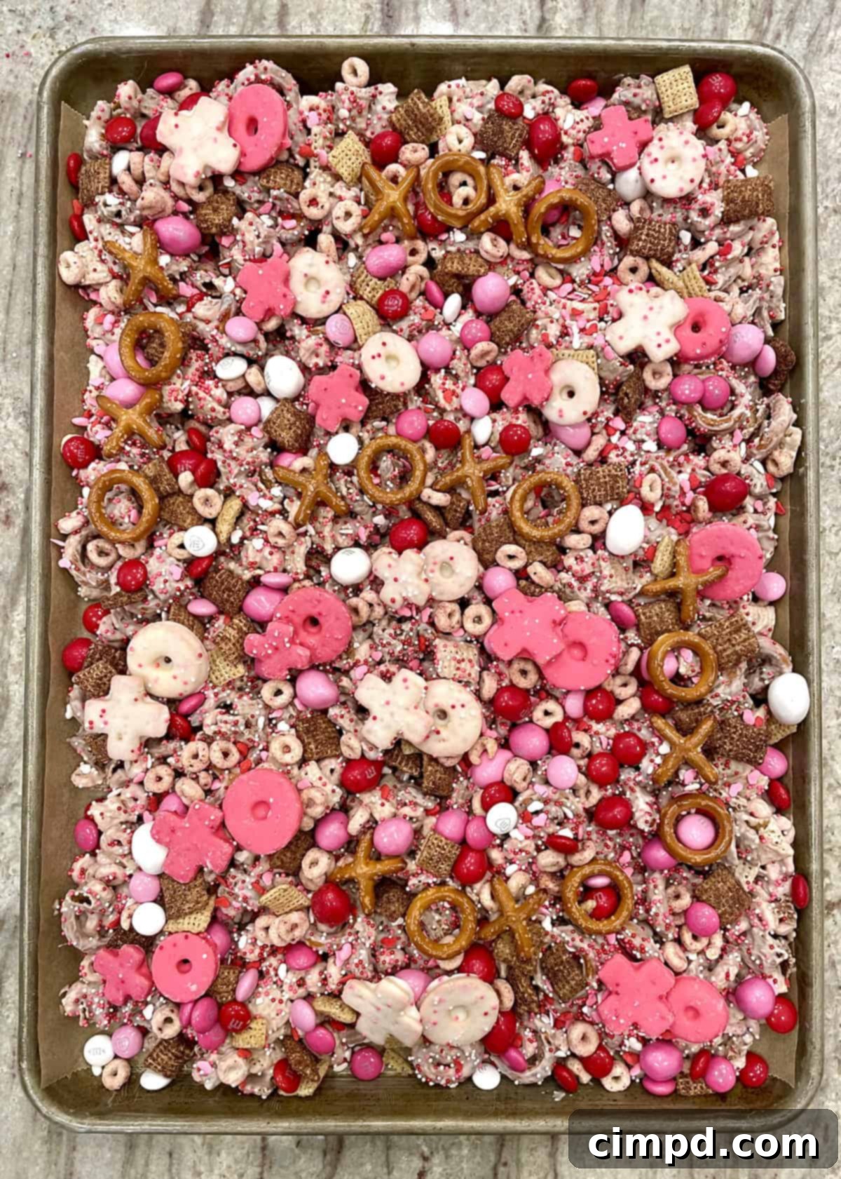 The finished XOXO Valentine's Day Snack Mix with all toppings, including candies, cereals, pretzels, and cookies, arranged on a baking sheet.