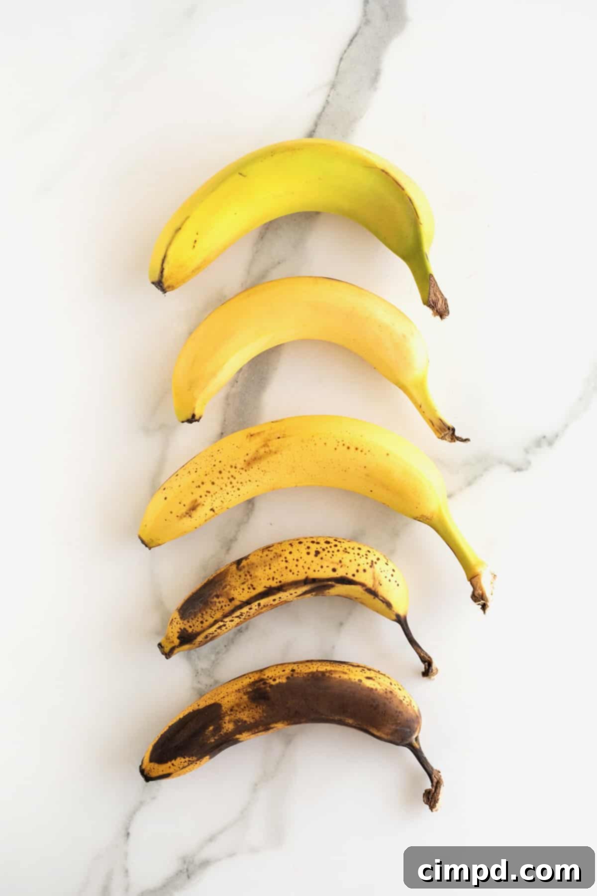 Bananas of varying ripeness on a white marble counter.