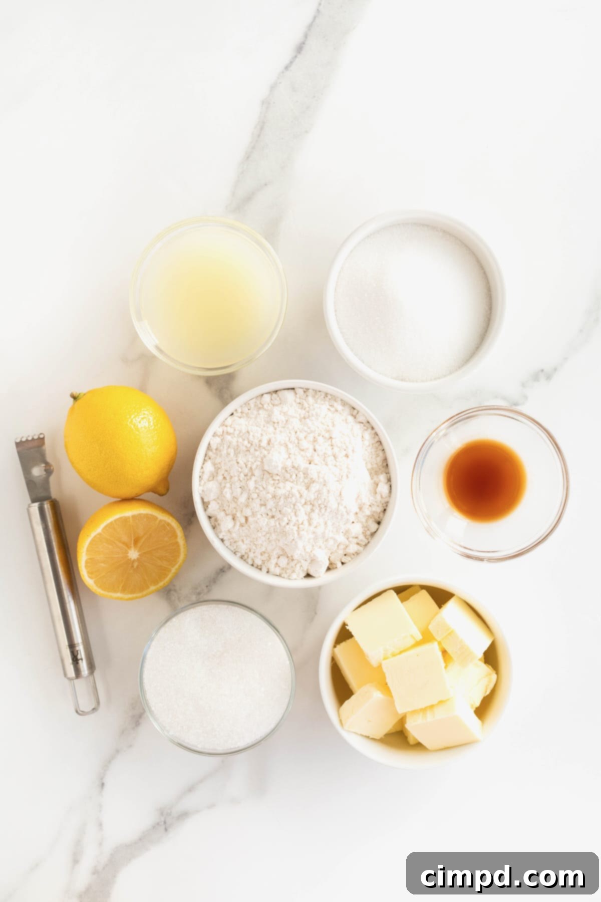 Ingredients to make lemon cookie displayed in small clear glass dishes on a pristine white marble counter, showcasing fresh lemons, flour, sugar, and butter.