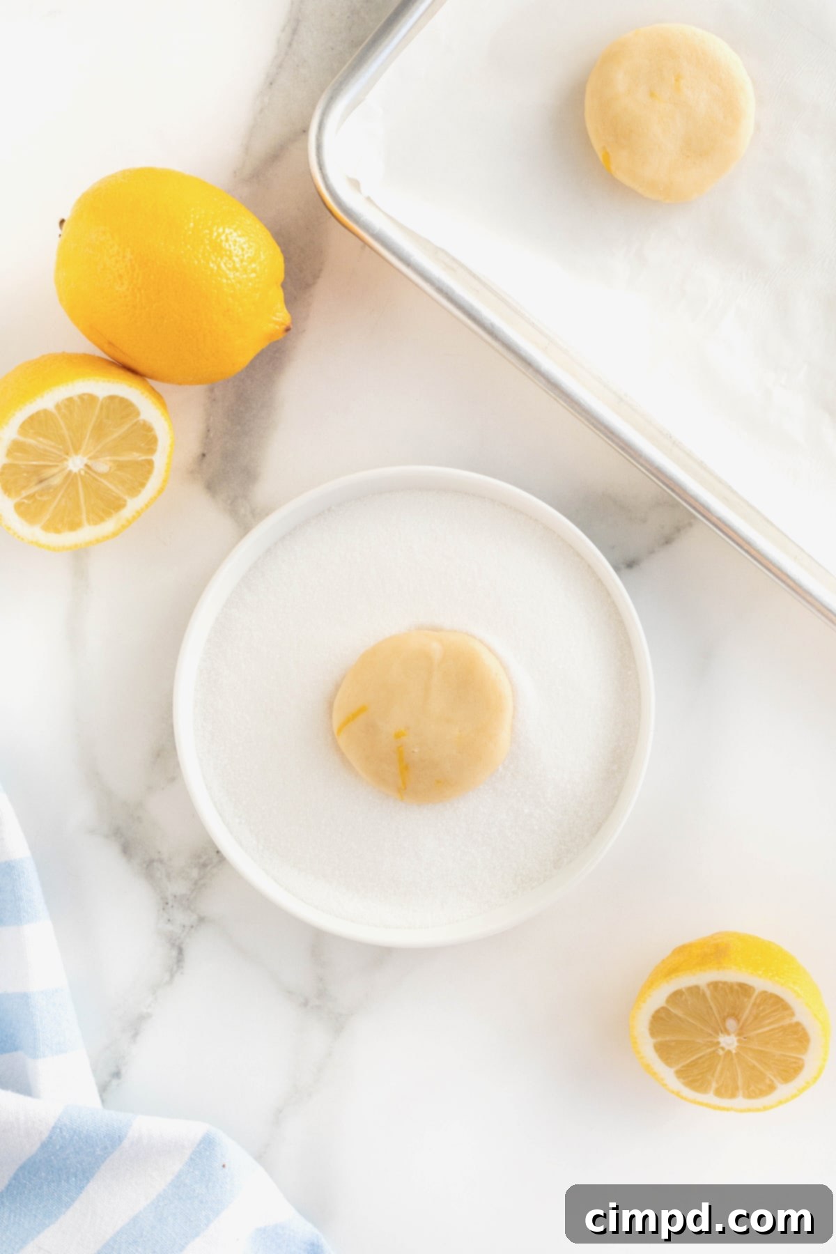 One flat, circular-shaped round of lemon cookie dough rests perfectly in a white, shallow, rimmed dish filled with granulated sugar, ready for its sweet coating.
