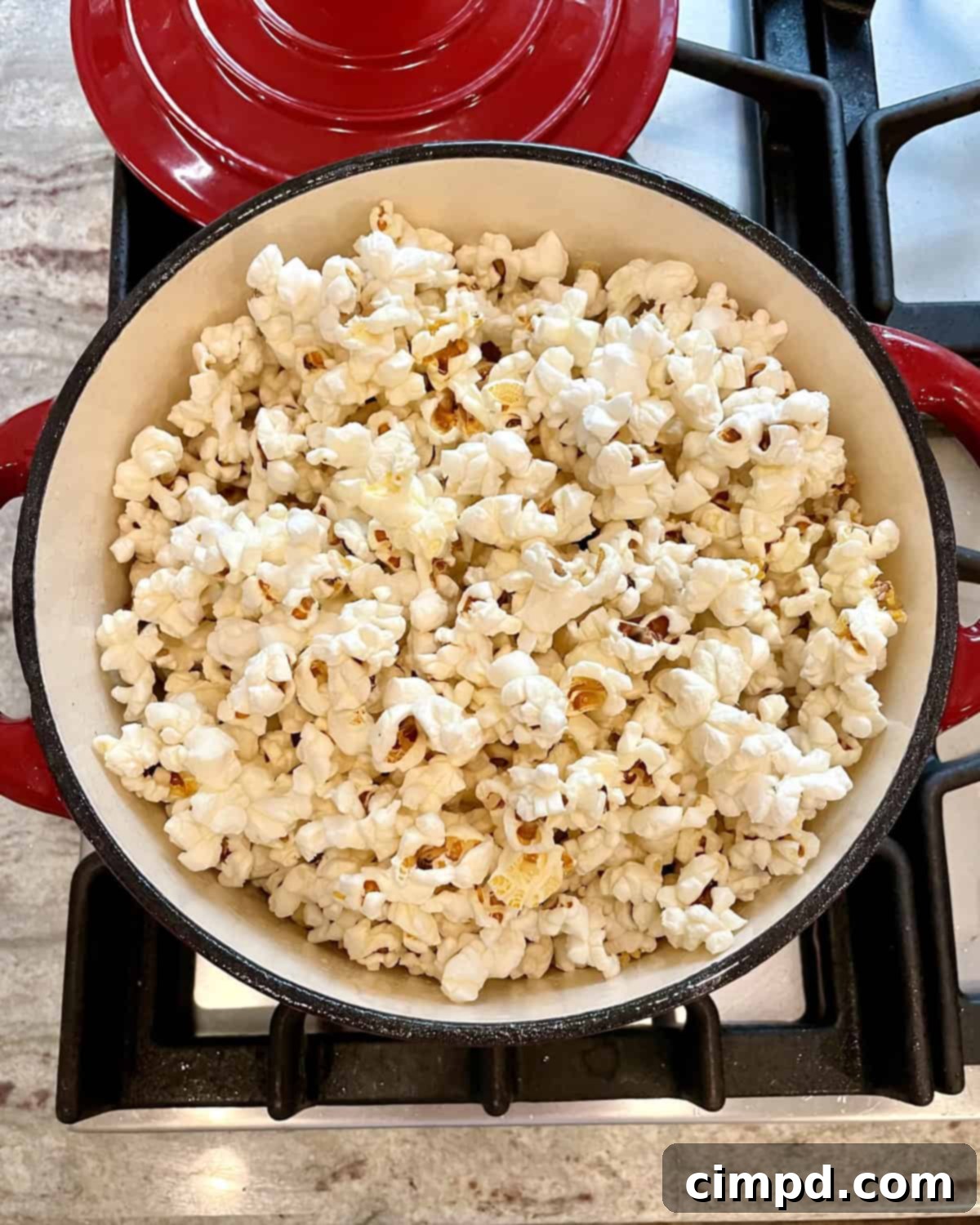 Popcorn Perfection From Your Stovetop 2 Bright red pot on a stovetop, brimming with freshly popped stovetop popcorn, ready to be enjoyed.