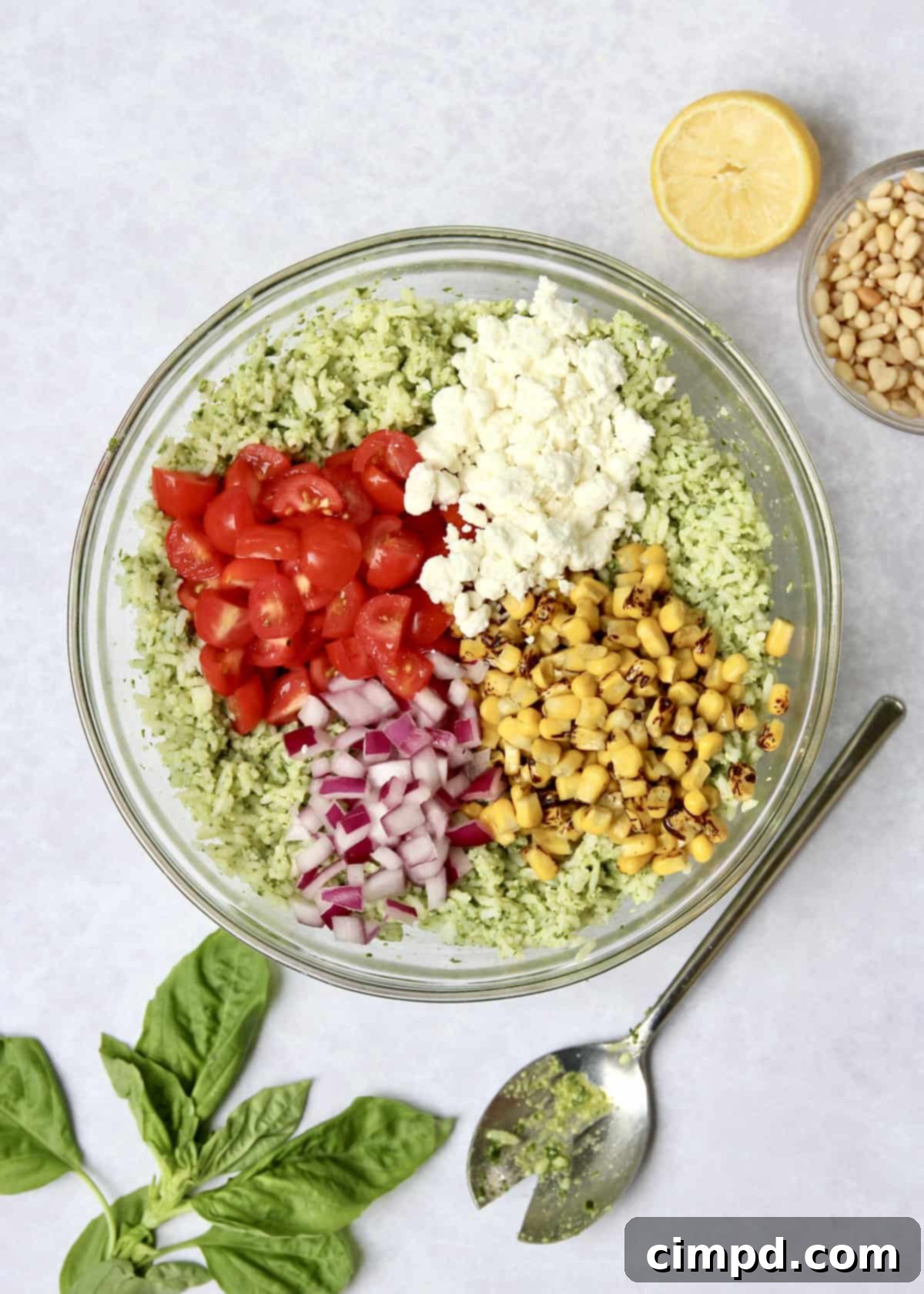 A Pesto Rice Salad being gently mixed in a large bowl with a serving spoon, showcasing its vibrant ingredients.