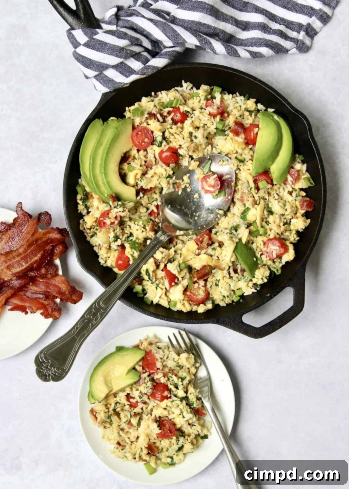 Cooked bacon, spinach, and tomatoes simmering in a skillet.