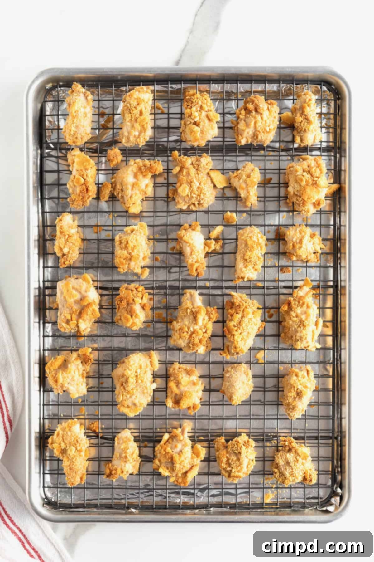 Baked chicken pieces coated in Ritz cracker crumbs, now golden brown and crispy, resting on a wire rack over a baking sheet.