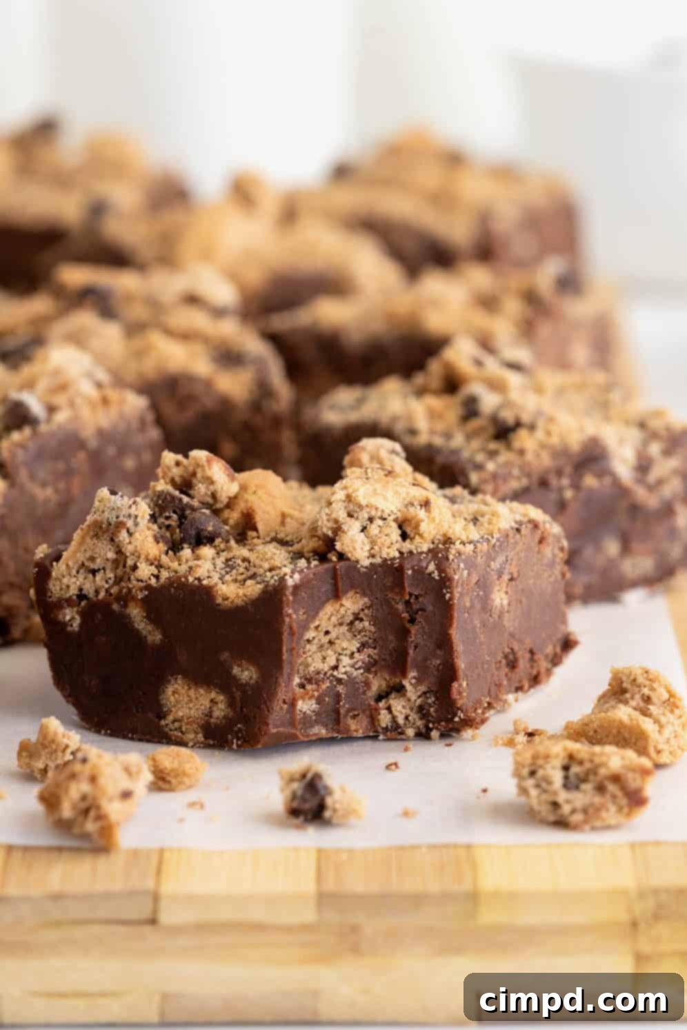 Several pieces of chocolate chip cookie fudge on a parchment lined surface, showcasing its creamy texture and embedded cookie pieces.