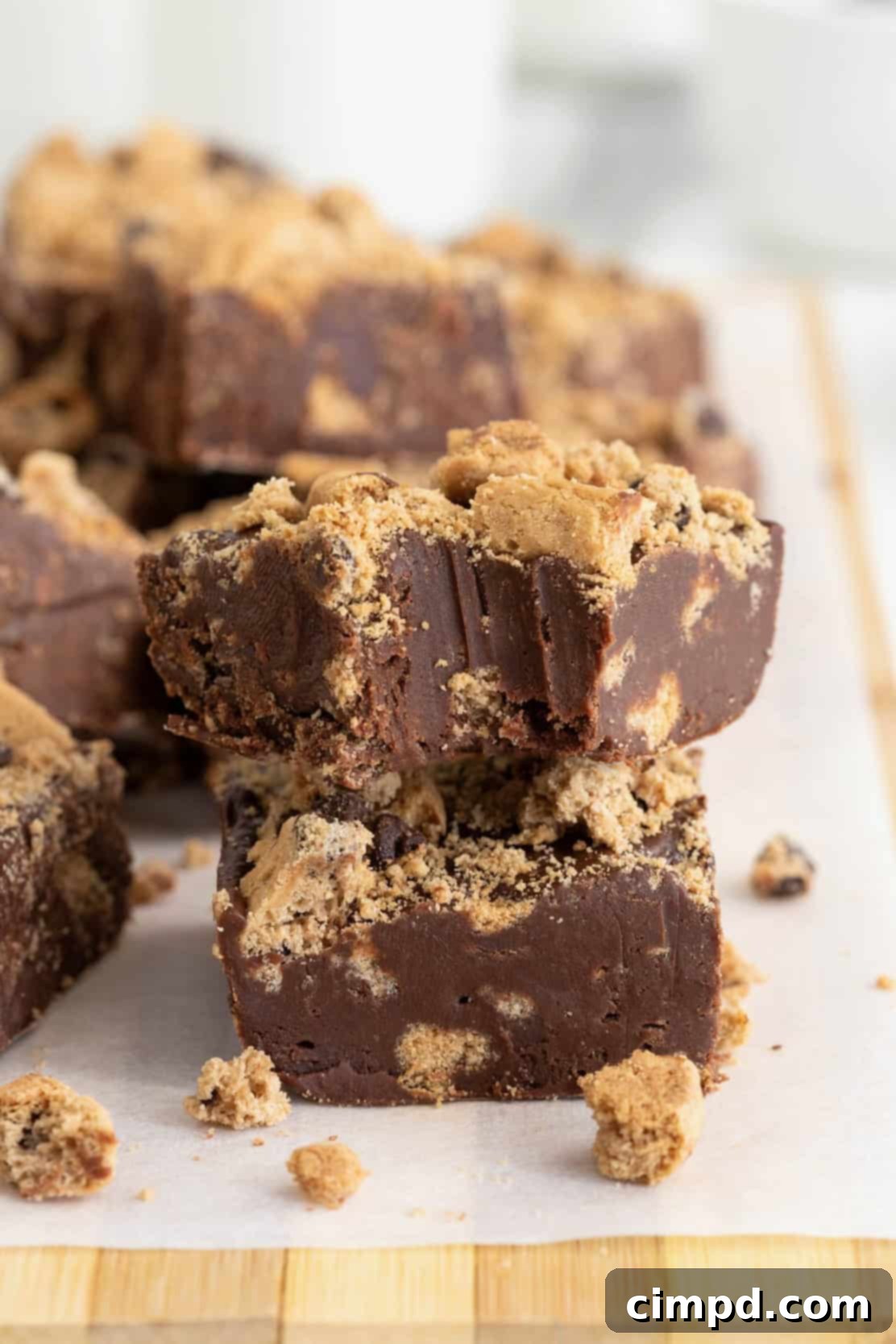 Chocolate fudge with chocolate chip cookies embedded in it on a parchment lined wooden cutting board, ready to be cut into squares.