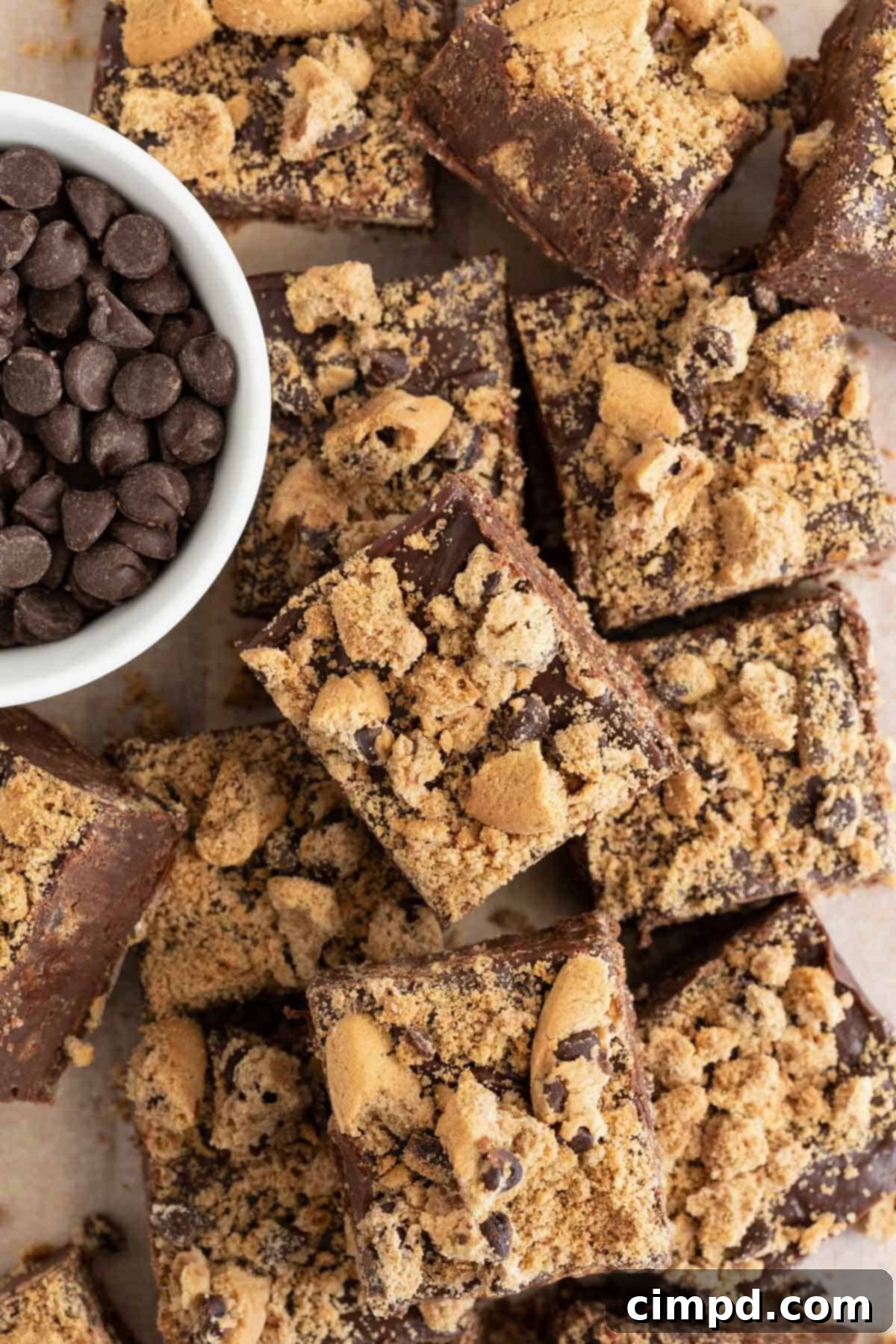 A pile of freshly made fudge squares next to a small white dish of semi-sweet chocolate chips, highlighting the ingredients.
