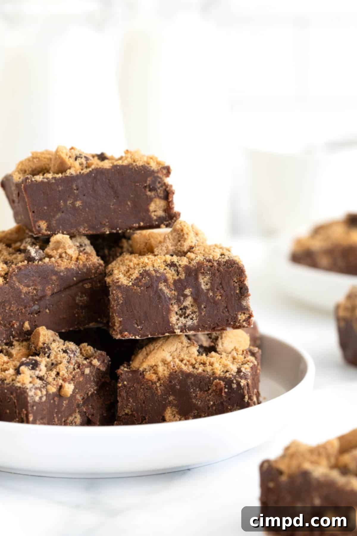 A neatly arranged pile of chocolate chip cookie fudge squares on a pristine white-rimmed plate, ready to be served.