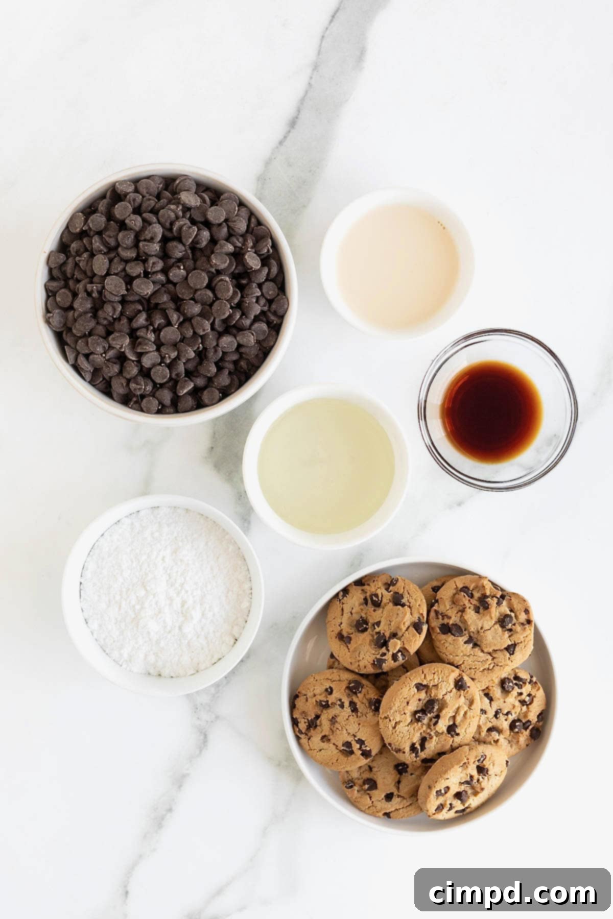 Ingredients to make chocolate chip cookie fudge displayed in small glass dishes on a pristine white marble counter, ready for preparation.