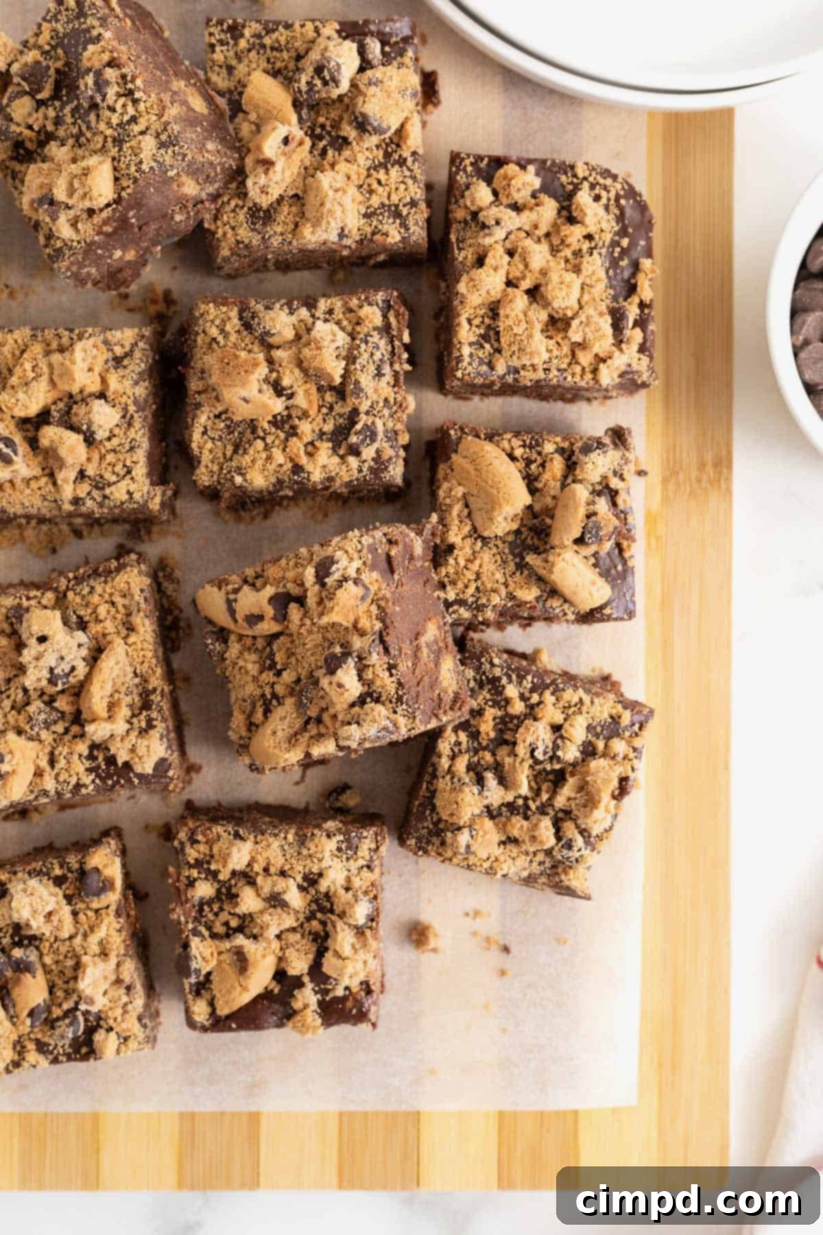 12 squares of chocolate chip cookie fudge neatly arranged on a parchment lined light wood cutting board, showcasing the final product.