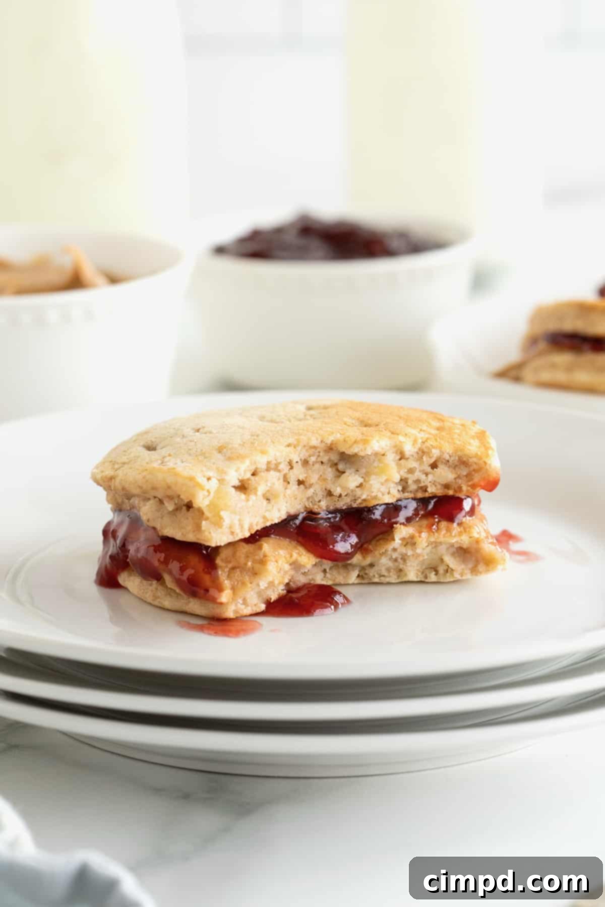 A banana pancake peanut butter and jelly sandwich on a small white plate. The sandwich has a bite out of it.