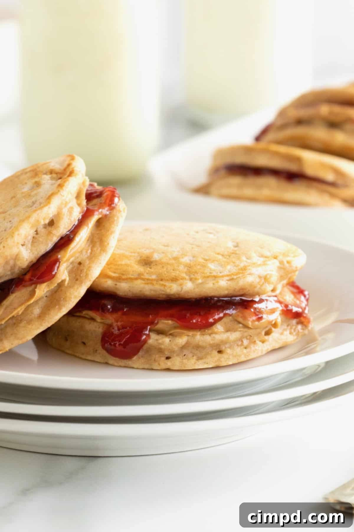 Two banana pancake peanut butter and jelly sandwiches on a small white plate.