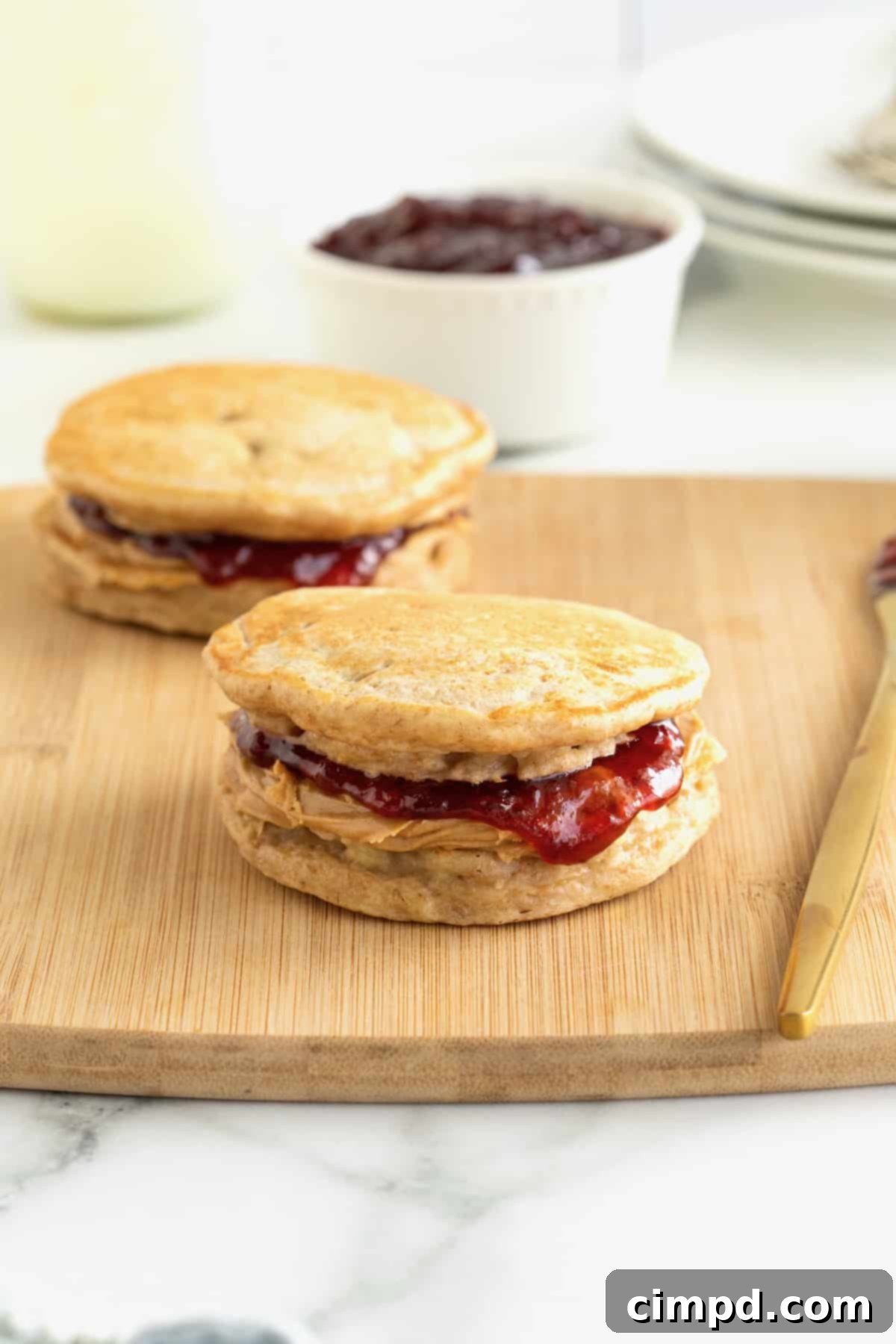 Two banana pancake peanut butter and jelly sandwiches on a wood cutting board.