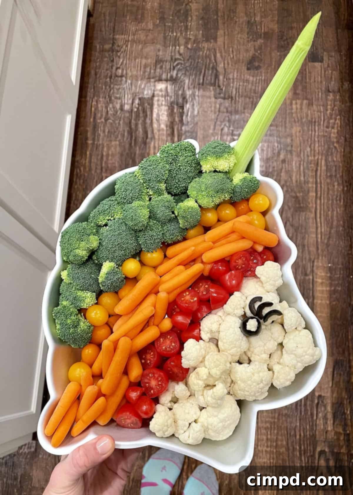 A creative Unicorn Veggie Tray featuring broccoli, yellow and red snacking tomatoes, carrots, and cauliflower florets arranged in a unicorn-shaped pan, complete with an olive eye and celery horn.