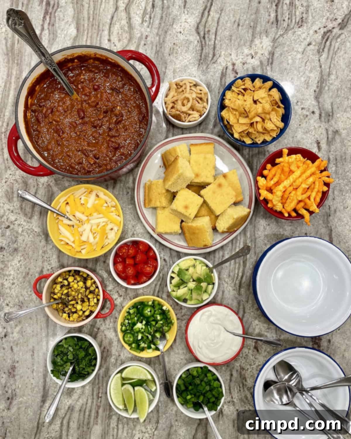 A beautifully arranged Fill-Your-Own Chili Bowl Spread, showcasing a rich chili, golden cornbread, and a variety of colorful toppings like cheese, avocado, and fresh cilantro, inviting guests to create their perfect bowl.