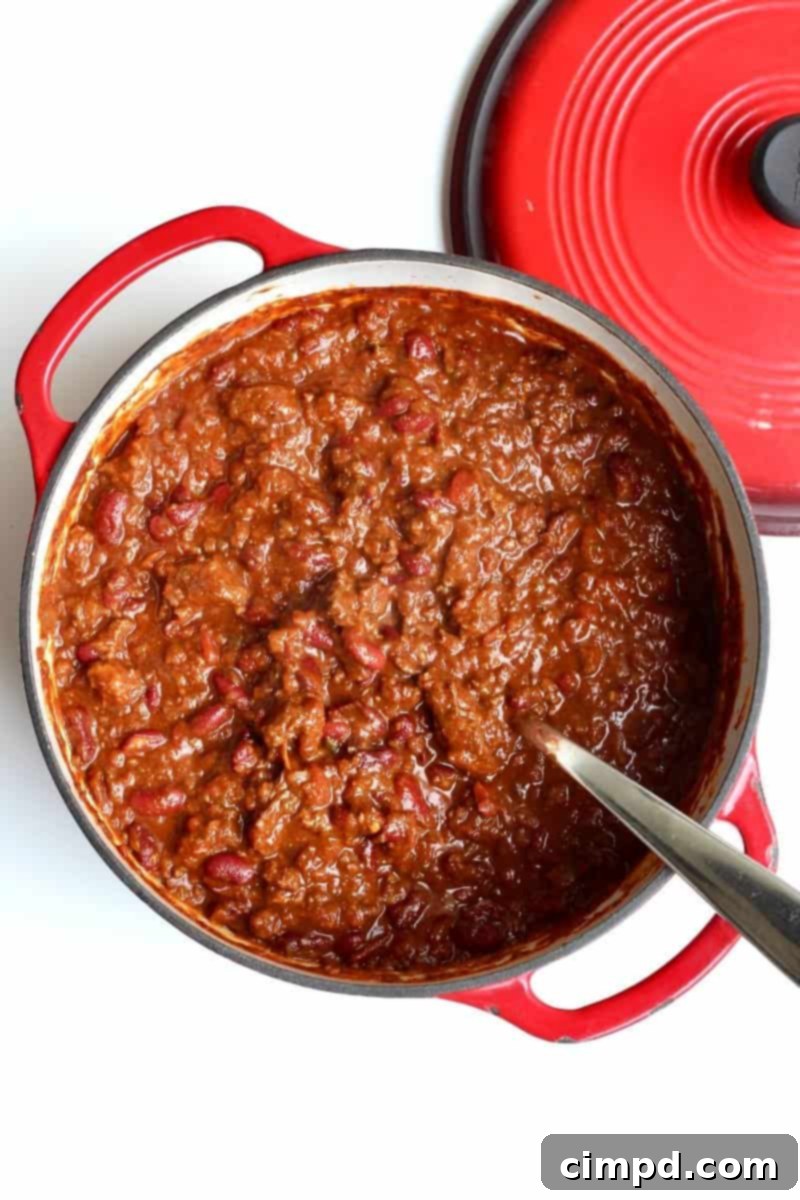 A close-up of a rich, steaming bowl of Brandon's Best Darn Chili, garnished with a swirl of sour cream and a sprinkle of fresh cilantro, emphasizing its hearty texture and appetizing appeal.
