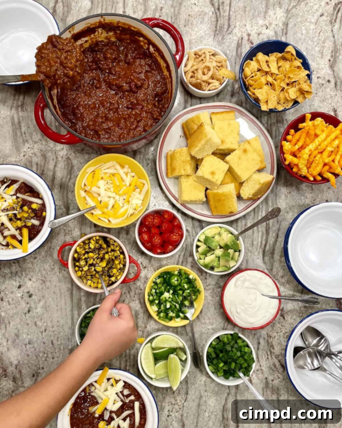 An overhead view of a diverse chili topping station, featuring bowls of shredded cheese, sour cream, diced avocado, cilantro, and crunchy corn chips, all ready for customization.