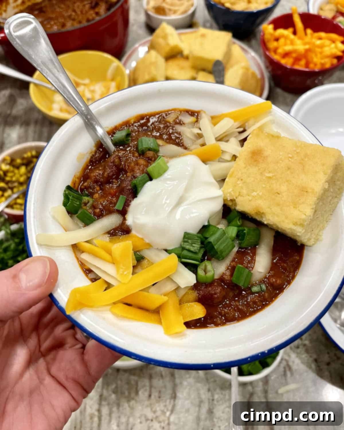 A guest's hand reaching for a bowl of chili, surrounded by an enticing spread of toppings, illustrating the interactive and customizable dining experience.