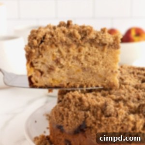 A slice of coffee cake with cinnamon sugar streusel on a pie server with a peach in the background.