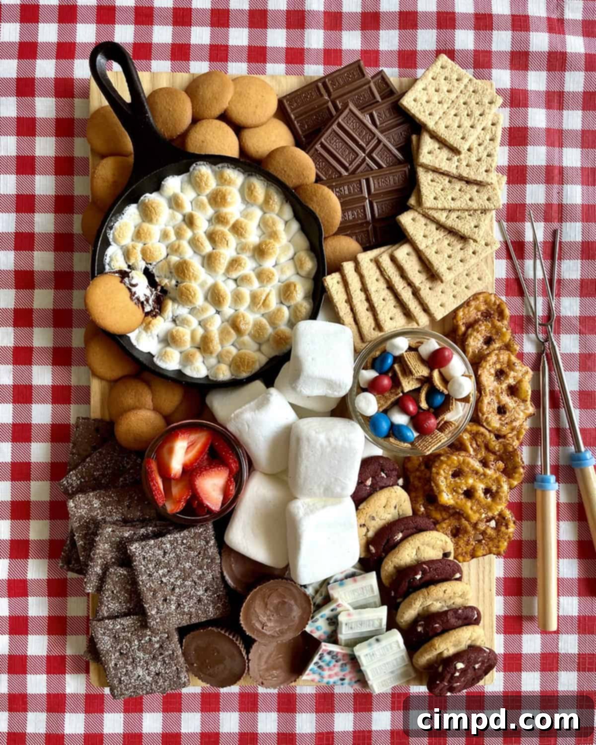 A wide shot of a lavish s'mores board, abundant with different types of graham crackers, chocolate bars, cookies, and a cast iron skillet of grilled s'mores dip.