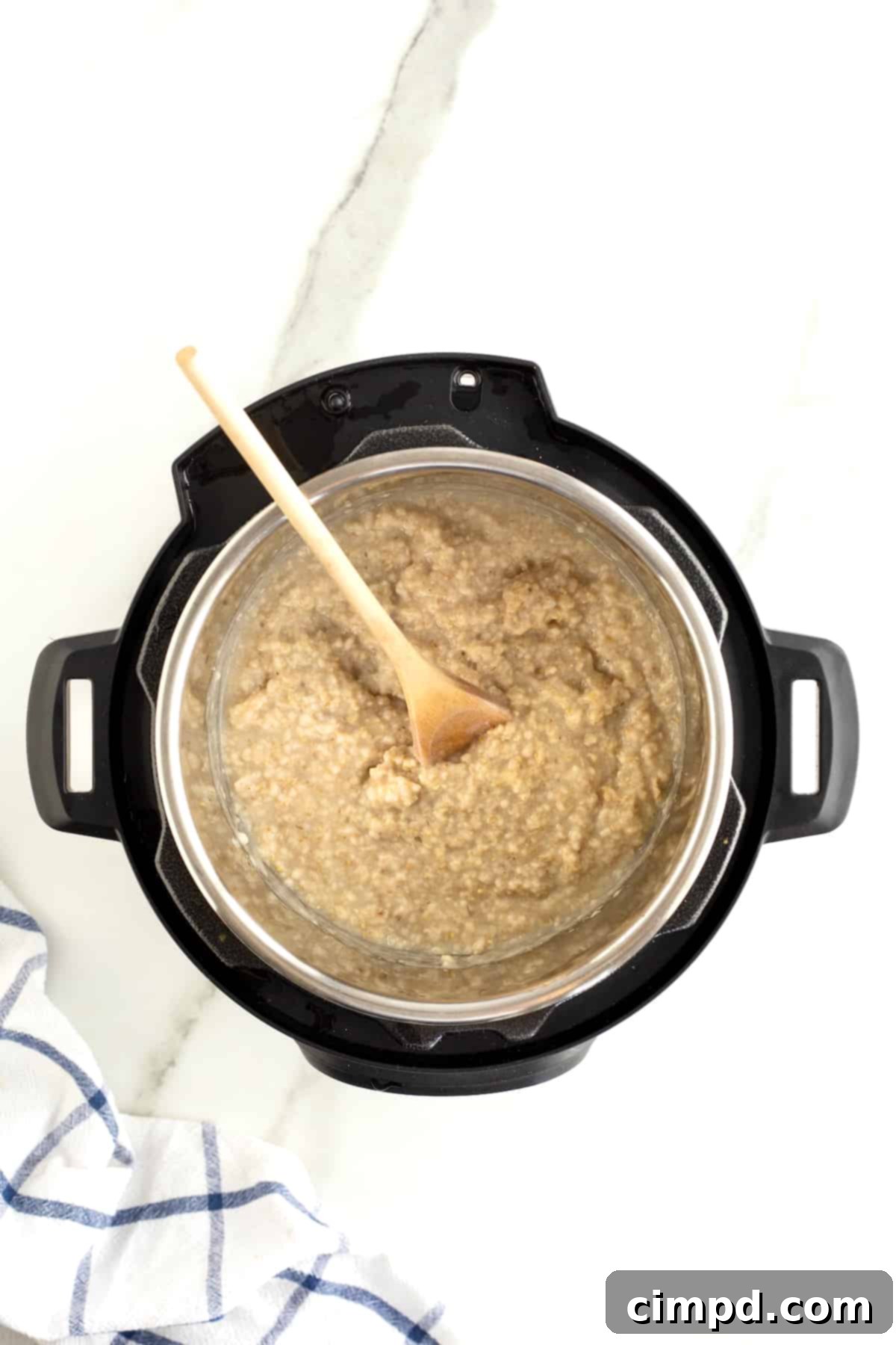 Perfect Steel Cut Oats Every Time 7 A wooden spoon gently stirs the creamy, cooked oatmeal within a pressure cooker, showcasing its perfect consistency after cooking.
