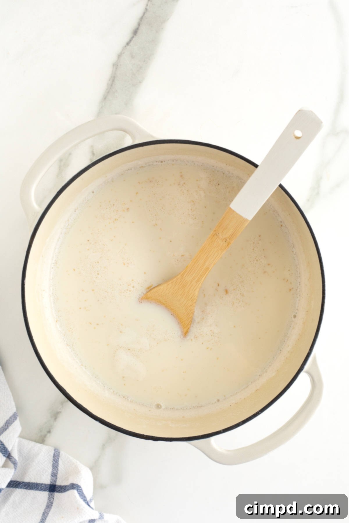 Perfect Steel Cut Oats Every Time 10 A pristine white Dutch oven rests on a stovetop, gently simmering a mixture of milk and oats, its contents slowly transforming into a comforting breakfast.