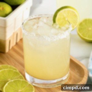 A salt rimmed glass filled with margarita on a rimmed wooden serving tray. There is a lime wedge on the rim of the glass.