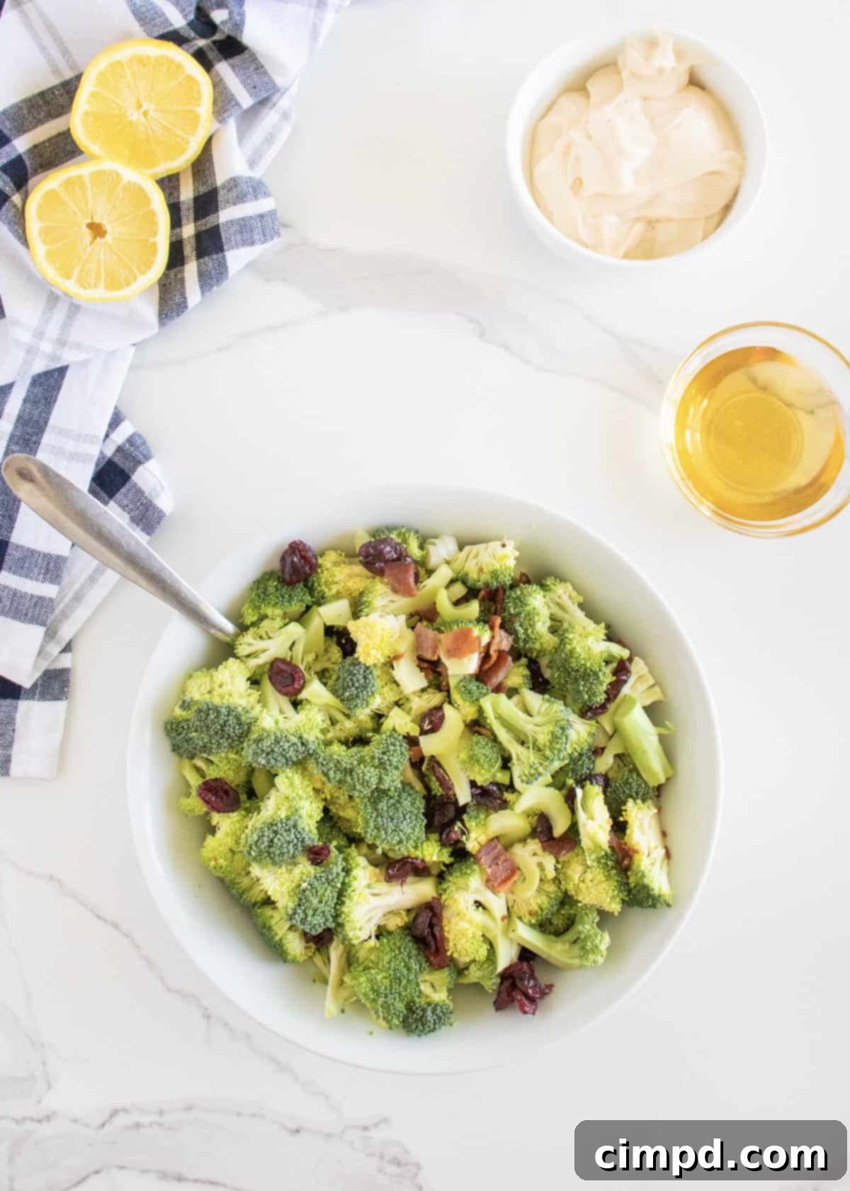 Broccoli, bacon bits, dried cranberries, and sliced green onions mixed together in a large white serving bowl.