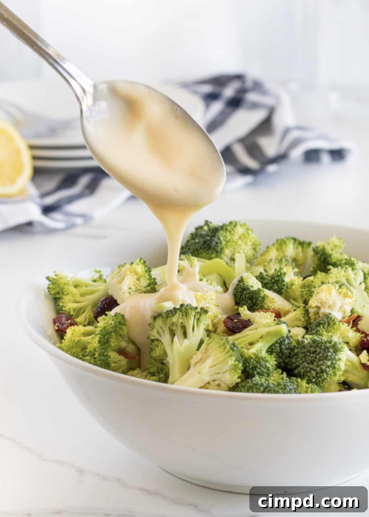 A creamy, tangy dressing being poured over the broccoli salad mixture in a large bowl.
