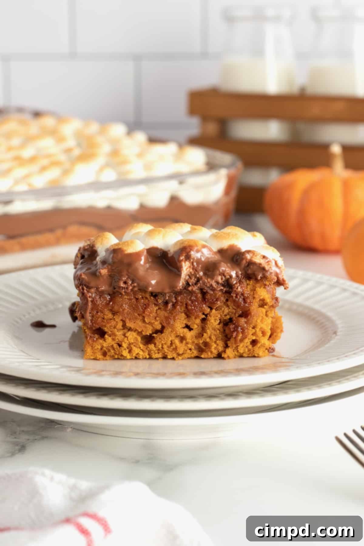 A festive Pumpkin S'mores Snack Cake by The BakerMama, topped with golden marshmallows and chocolate drizzle.