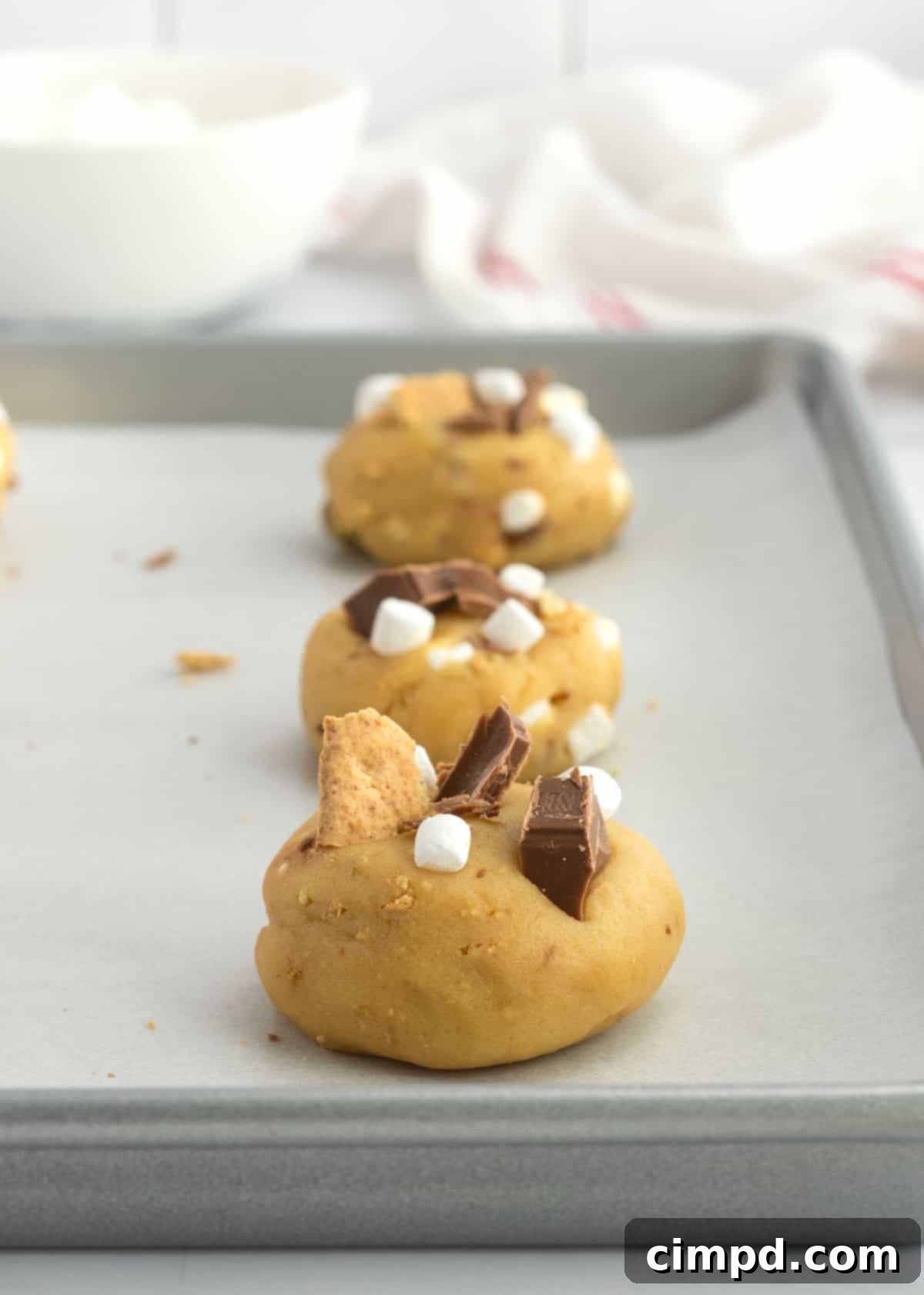 Dreamy Smores Pudding Cookies 7 Cookie dough balls on a baking sheet, topped with extra s'mores ingredients for a perfect finish.