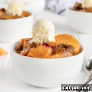 White bowl filled with peach crumble with a small scoop of vanilla ice cream on top.