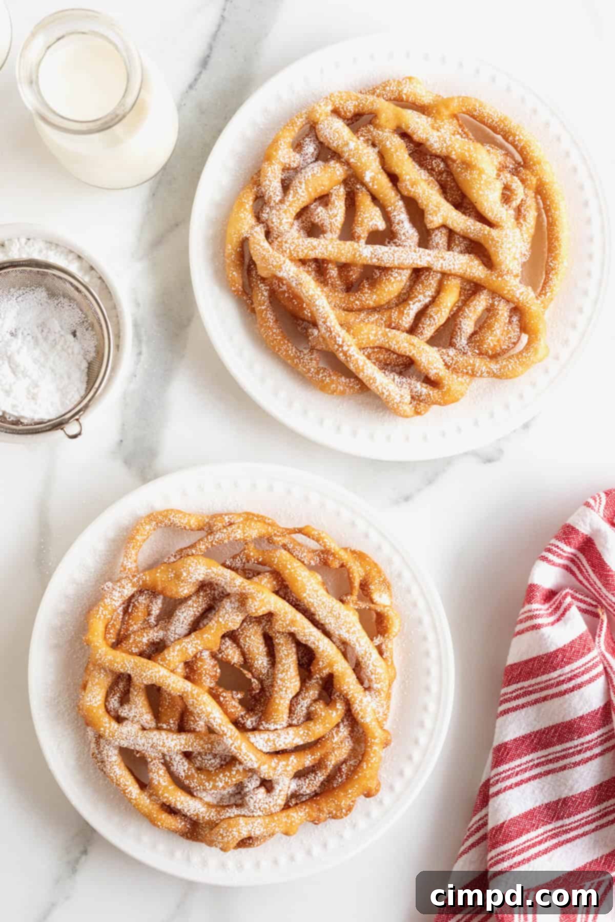 Two golden homemade funnel cakes generously topped with white powdered sugar, served on pristine white plates.