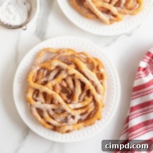 Two funnel cakes topped with powdered sugar on white plates.