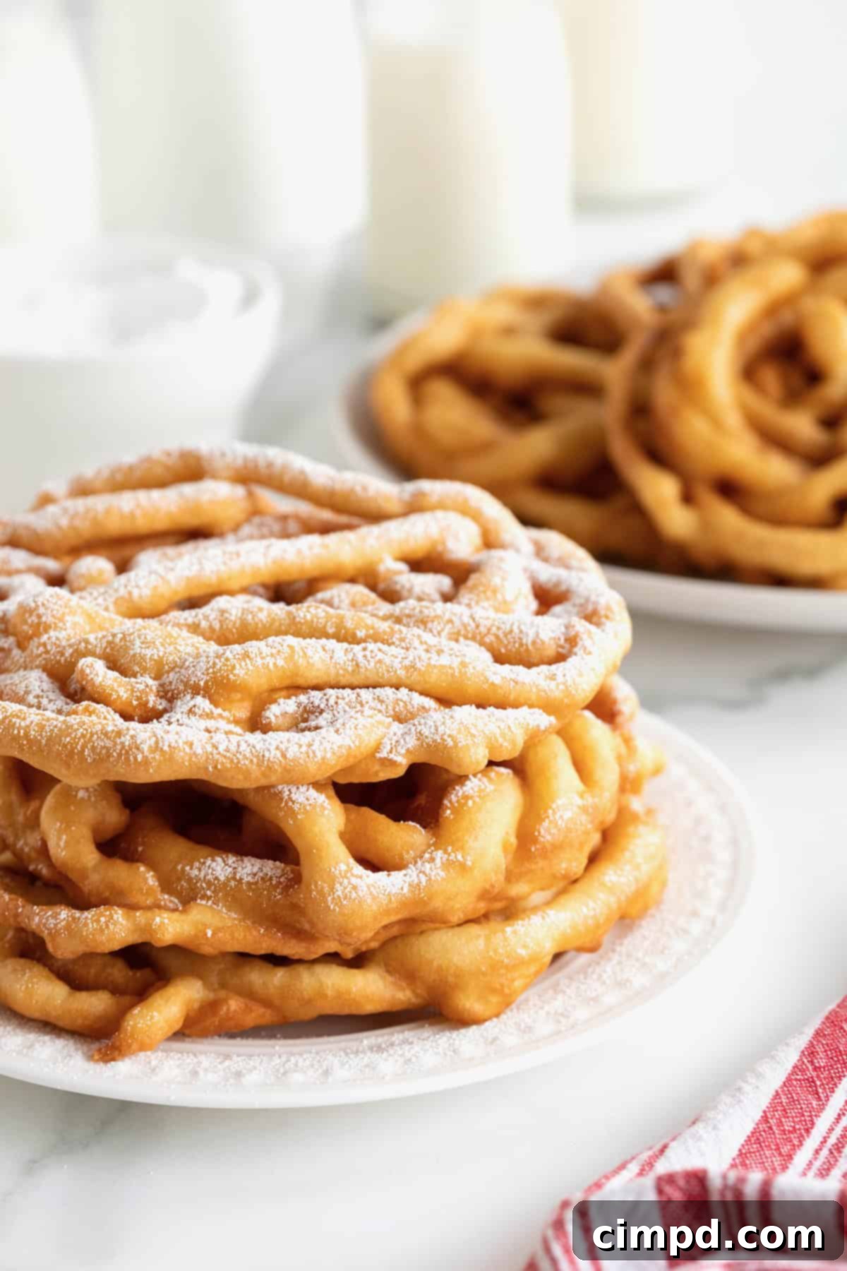 Two freshly prepared homemade funnel cakes, beautifully dusted with a fine layer of powdered sugar, presented on a white serving plate.