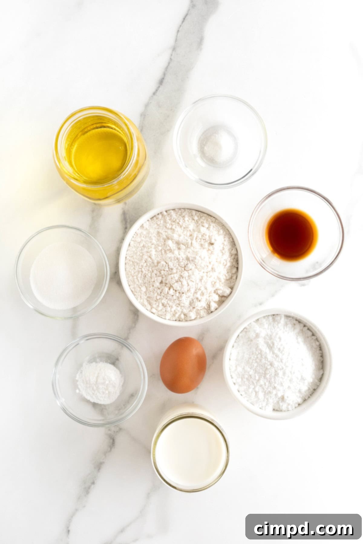 Individual ingredients for homemade funnel cakes neatly arranged in small glass dishes on a pristine white marble countertop.