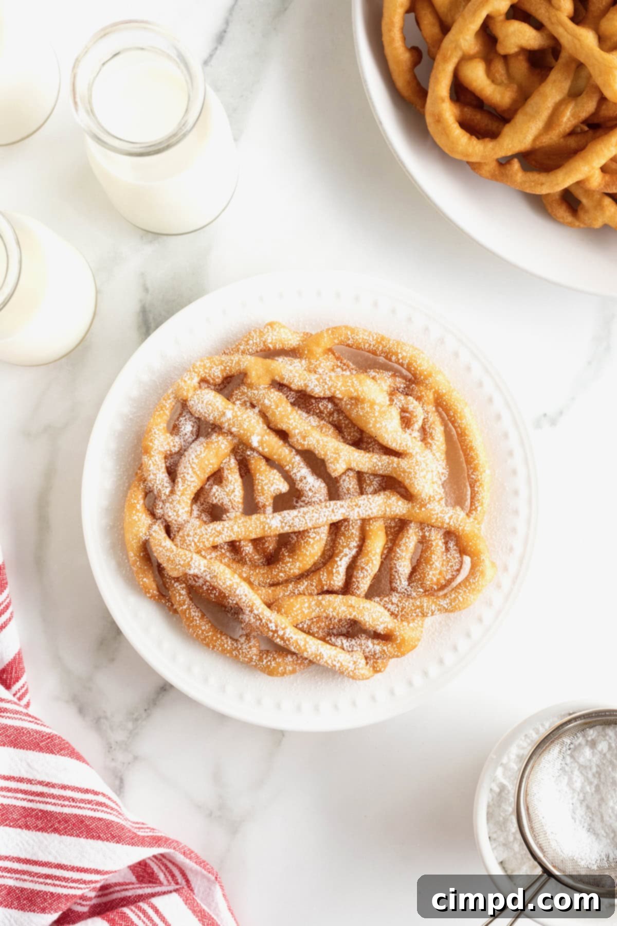 A single, perfectly fried homemade funnel cake, generously topped with white powdered sugar, served on a round white plate.