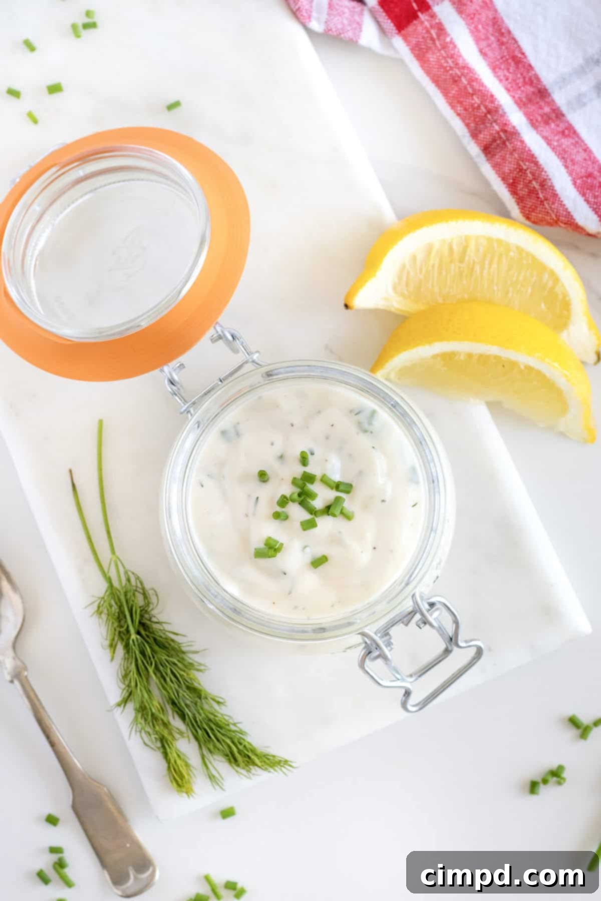A glass jar of homemade ranch dressing on a white marble cutting board. To the right are two lemon wedges. 