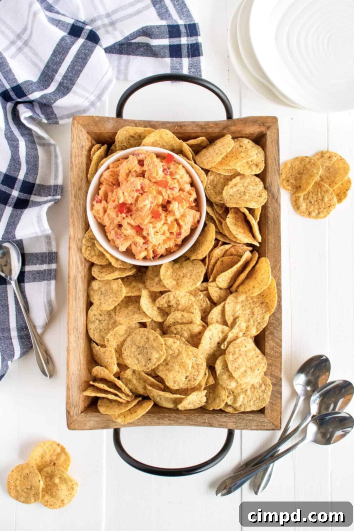 A beautifully presented Pimento Cheese Dip on a wooden tray, surrounded by an assortment of crispy chips, ready for serving at a gathering.